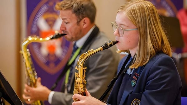 Dos estudiantes tocan el saxofón en el escenario de la St. Leonards School frente a un fondo morado.