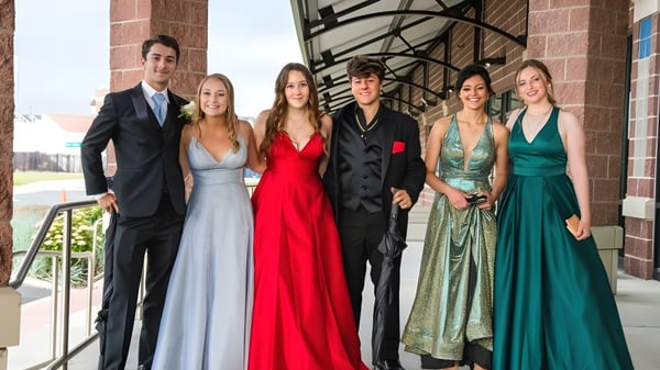 Seis estudiantes de la St. Louis Community School posan con ropa formal frente a un edificio de ladrillo con detalles arquitectónicos.