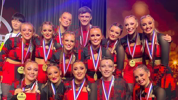 Un grupo de estudiantes de la St. Louis Secondary School Dundalk posan con trajes rojos y negros en el escenario.