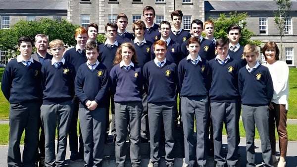 Un grupo de estudiantes en uniformes escolares está de pie en el césped frente a un edificio de ladrillo del St. Macartan's College.