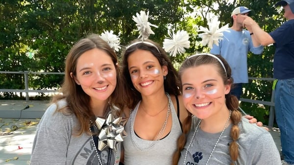 Tres alumnas de St. Margaret's School posan afuera frente a árboles verdes y arbustos.