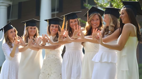 Un grupo de jóvenes mujeres en togas de graduación blancas celebra juntas en el campus de la St. Margaret’s School.