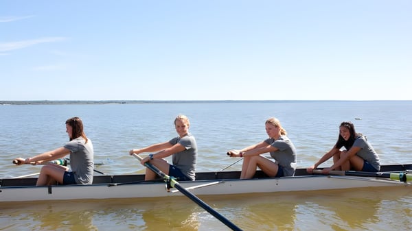 Cuatro personas están sentadas en un bote en el agua en el campus de St. Margaret's School bajo un cielo despejado.