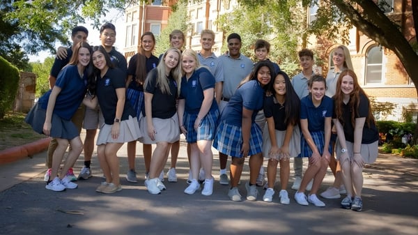Un grupo de estudiantes está juntos afuera frente a un edificio de ladrillo en el campus de la St. Mary Catholic High School.