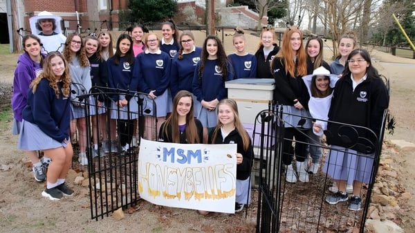 Un grupo de estudiantes de la St. Mary Catholic High School está con un banner frente a un edificio de ladrillo.