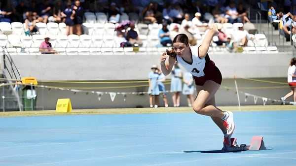 Una deportista de la St. Mary's Anglican Girls' School realiza un ejercicio de gimnasia sobre una colchoneta azul frente a espectadores.