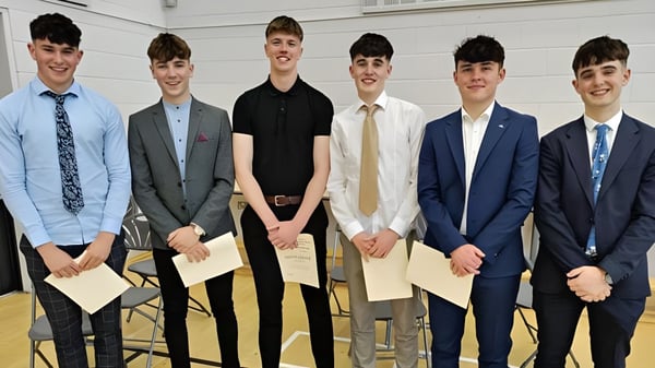 Un grupo de seis jóvenes en traje está de pie juntos frente a un fondo blanco en el campus de St. Mary’s College.