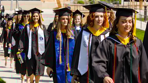 Un grupo de graduadas y graduados del St Mary’s District & Vocational Collegiate Institute está de pie con vestimenta académica en el campus.