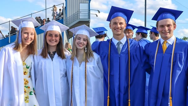 Los graduados de la St. Mary's High School en togas azules están frente a un edificio escolar bajo un cielo azul.