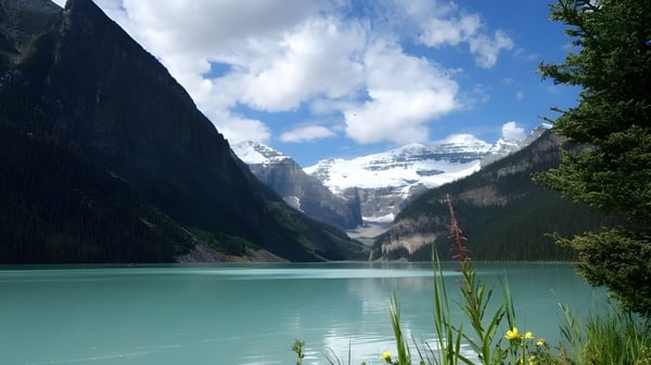 Un tranquilo lago alpino con montañas cubiertas de nieve y vegetación verde cerca de la St. Mary's High School.