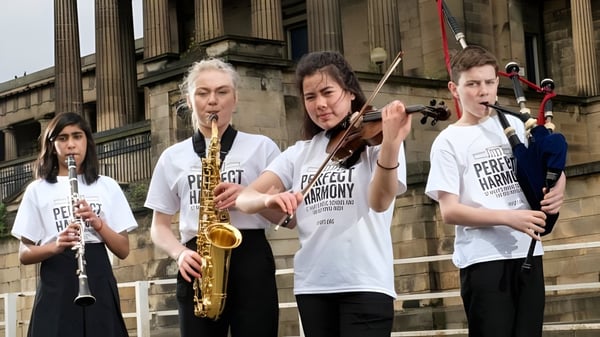Un grupo de jóvenes músicos toca diferentes instrumentos frente al edificio clásico de la St. Mary’s Music School.