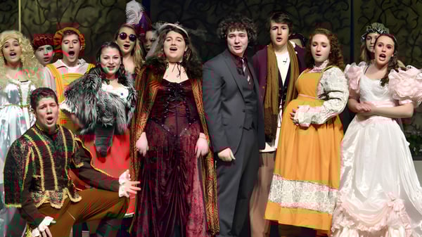 Estudiantes de St. Mary's Ryken High School presentan una obra de teatro en coloridos trajes en un escenario con fondo oscuro.