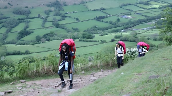 Tres estudiantes de la St. Mary’s School Ascot caminan por un camino de campo a través de un paisaje de colinas verdes.