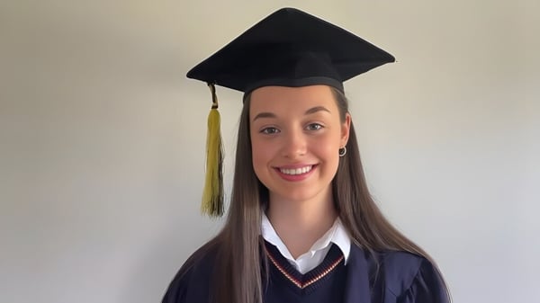 Una graduada de St. Mary’s Secondary con birrete y toga frente a un fondo blanco.