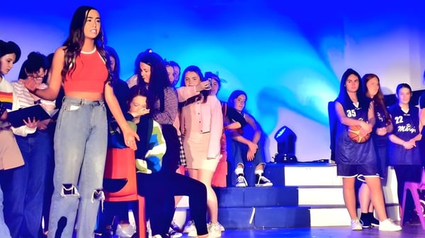 Un grupo de alumnas de la St. Mary’s Secondary School Baldoyle está en un escenario con iluminación colorida.