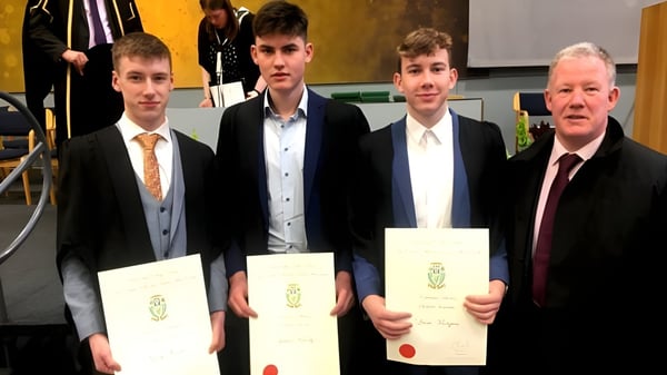 Los graduados de St. Mel’s College en atuendo formal sostienen sus diplomas durante la ceremonia de graduación con un invitado de honor.