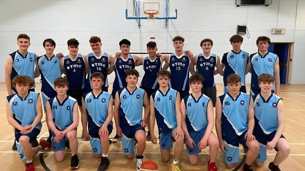Un grupo de estudiantes de St. Michael's College posan en el gimnasio frente a una canasta de baloncesto.