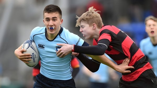 Dos jugadores de rugby luchan en el campo del St. Michael's College, uno lleva una camiseta azul claro, el otro rojo-negro.