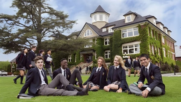 Estudiantes de la St. Michaels University School están sentados en uniforme escolar en la pradera frente al edificio principal cubierto de hiedra.