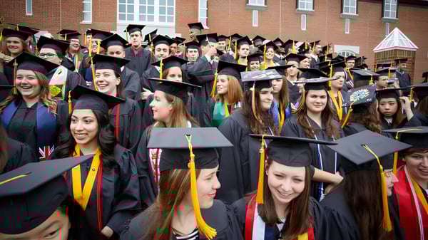 Un gran grupo de graduados en vestimenta académica celebra frente al edificio de ladrillo en el campus de la St. Michaels University School.