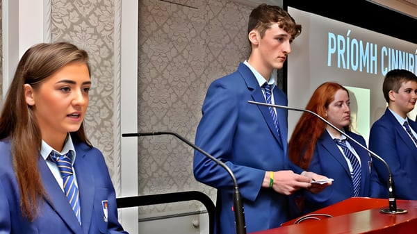 Un grupo de estudiantes del St. Mogues College está frente a un fondo con la inscripción Priory Church.