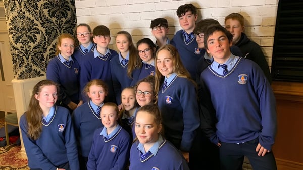 Un grupo de estudiantes en uniformes escolares azules posan frente a una pared decorada en el campus del St. Mogues College.