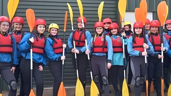 Alumnos del St. Patricks College en Cork están frente a un edificio de metal y sostienen palas de colores durante el entrenamiento de kayak.