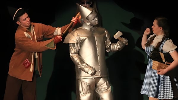 Tres estudiantes de St. Patrick's High School en trajes de teatro en un escenario oscuro.