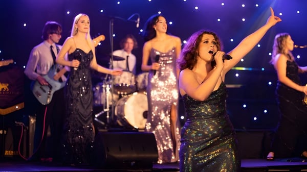 Un grupo de actrices de St Paul’s School canta y baila en el escenario con luces brillantes de fondo.