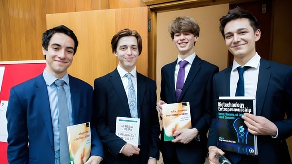 Cuatro estudiantes de la St. Paul’s School están en un entorno empresarial con libros y documentos.