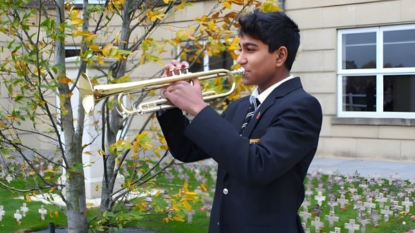 Un estudiante de la St. Paul’s School toca un instrumento de metal frente a un paisaje otoñal y un edificio escolar.