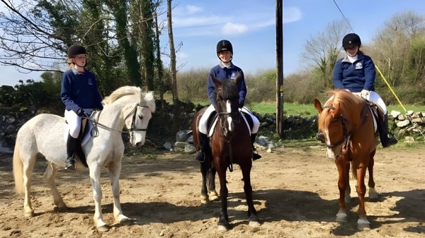 Tres alumnos de la St. Paul's Secondary en Galway montan a caballo en un sendero del bosque con árboles y vegetación al fondo.