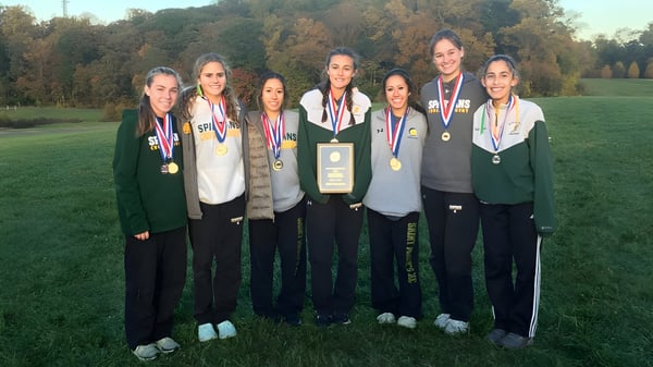 Un grupo de jóvenes atletas de la St. Peter High School está con medallas en un campo de césped frente a unos árboles.