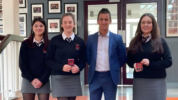 Cuatro personas en ropa formal están en el pasillo de St. Peter's Community School junto a imágenes decorativas en la pared.