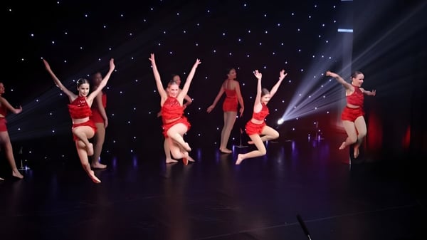 Un grupo de bailarines en trajes rojos presenta una coreografía en el escenario de la St. Peters School bajo un cielo estrellado.