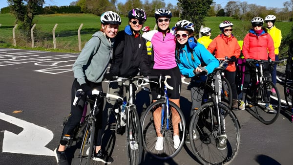 Un grupo de estudiantes de la St. Raphaela’s Secondary School en colorido atuendo de ciclismo posan en una calle frente a un prado verde.