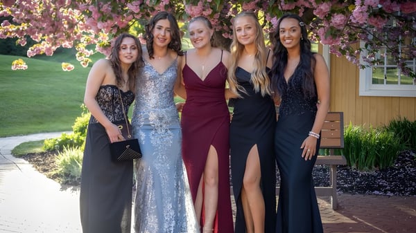 Cinco estudiantes de la St. Raphaela’s Secondary School posan juntas en un jardín con árboles en flor.
