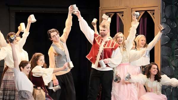 Alumnos de la St. Rose High School realizan una actuación en el escenario con coloridos disfraces sobre un fondo oscuro.