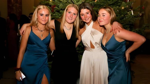 Cuatro alumnas de St. Teresa’s College posan frente a un árbol de Navidad decorado.