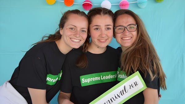 Tres estudiantes de la St. Thomas High School sonríen y posan frente a una pared color turquesa con guirnaldas coloridas.