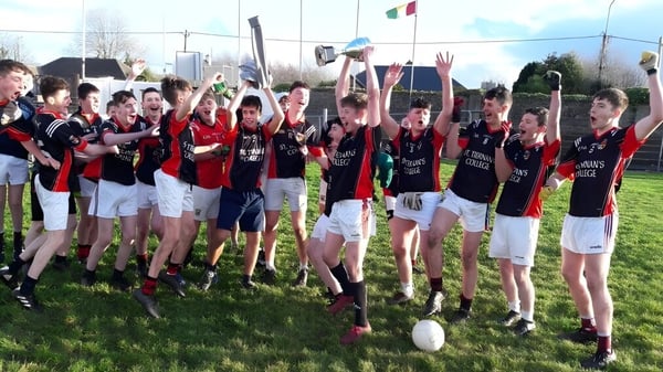 Alumnos de St. Tiernan’s College celebran juntos en sus uniformes deportivos en un campo de deportes con un estadio al fondo.