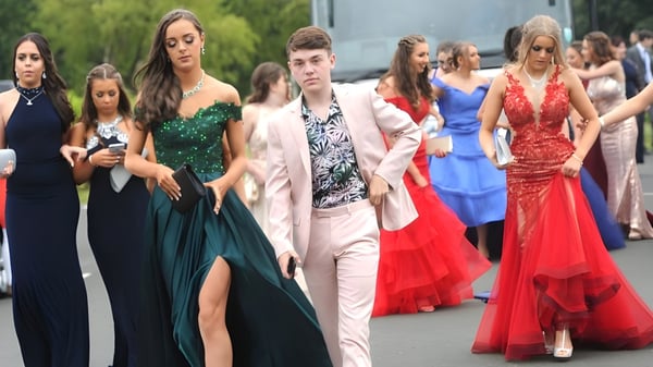 Un grupo de alumnas y alumnos elegantemente vestidos de St. Tiernan’s College se reúne al aire libre frente a árboles y edificios.