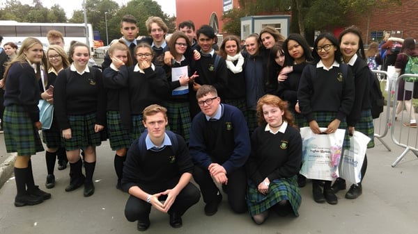Un gran grupo de alumnas y alumnos de St. Tiernan’s College está reunido frente a un edificio escolar al aire libre.