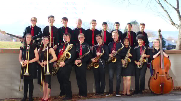 Un grupo de músicos en ropa formal posan con sus instrumentos frente a un edificio en el campus de St. Vrain Valley Schools.