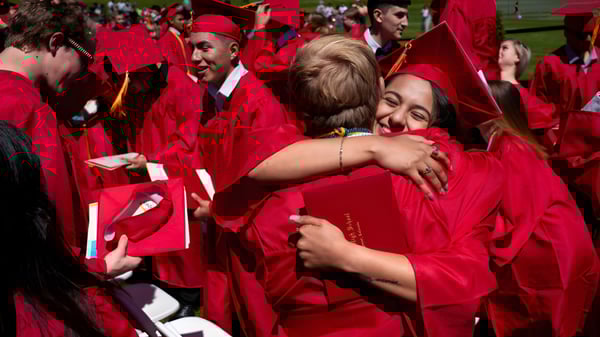 Un grupo de graduados en togas rojas se abrazan en un prado en el campus de St. Vrain Valley Schools.