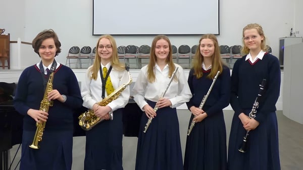 Cinco alumnas en uniformes de Stamford Endowed Schools están juntas con una flautista frente a una pantalla de proyección.
