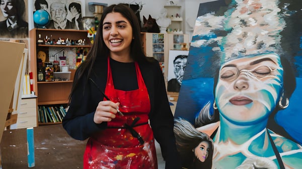 Una estudiante de Stamford High School está frente a un aula de arte con muchas obras de arte y estanterías.
