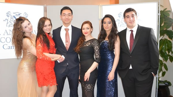 Seis personas posan en un evento en el campus del St. Andrew’s College Cambridge frente a un fondo de AMCHAM.