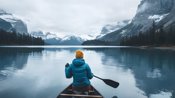 Una persona con chaqueta azul y sombrero rema en una canoa sobre un lago espejo con montañas nevadas de fondo en el campus del Stanstead College.