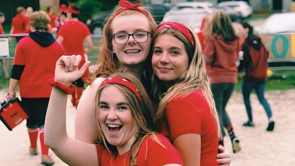 Tres alumnas del Stayner Collegiate Institute llevan camisetas rojas y sonríen frente a una multitud.